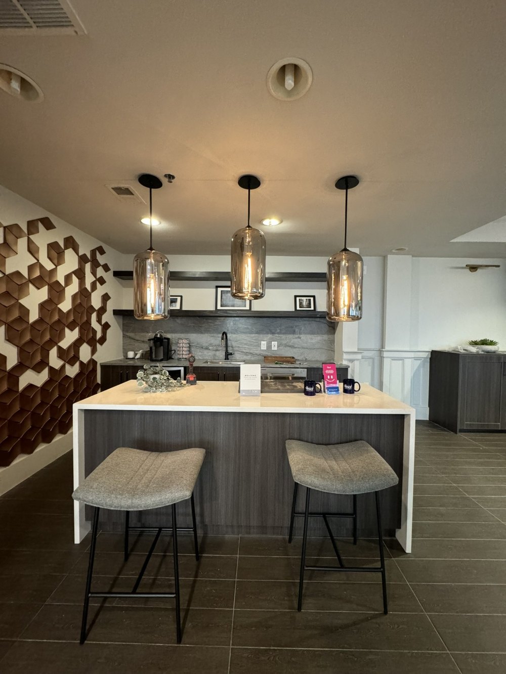 Commercial amenity kitchen with dark wood-grain cabinets and a waterfall island, built by X-Trim Cabinets