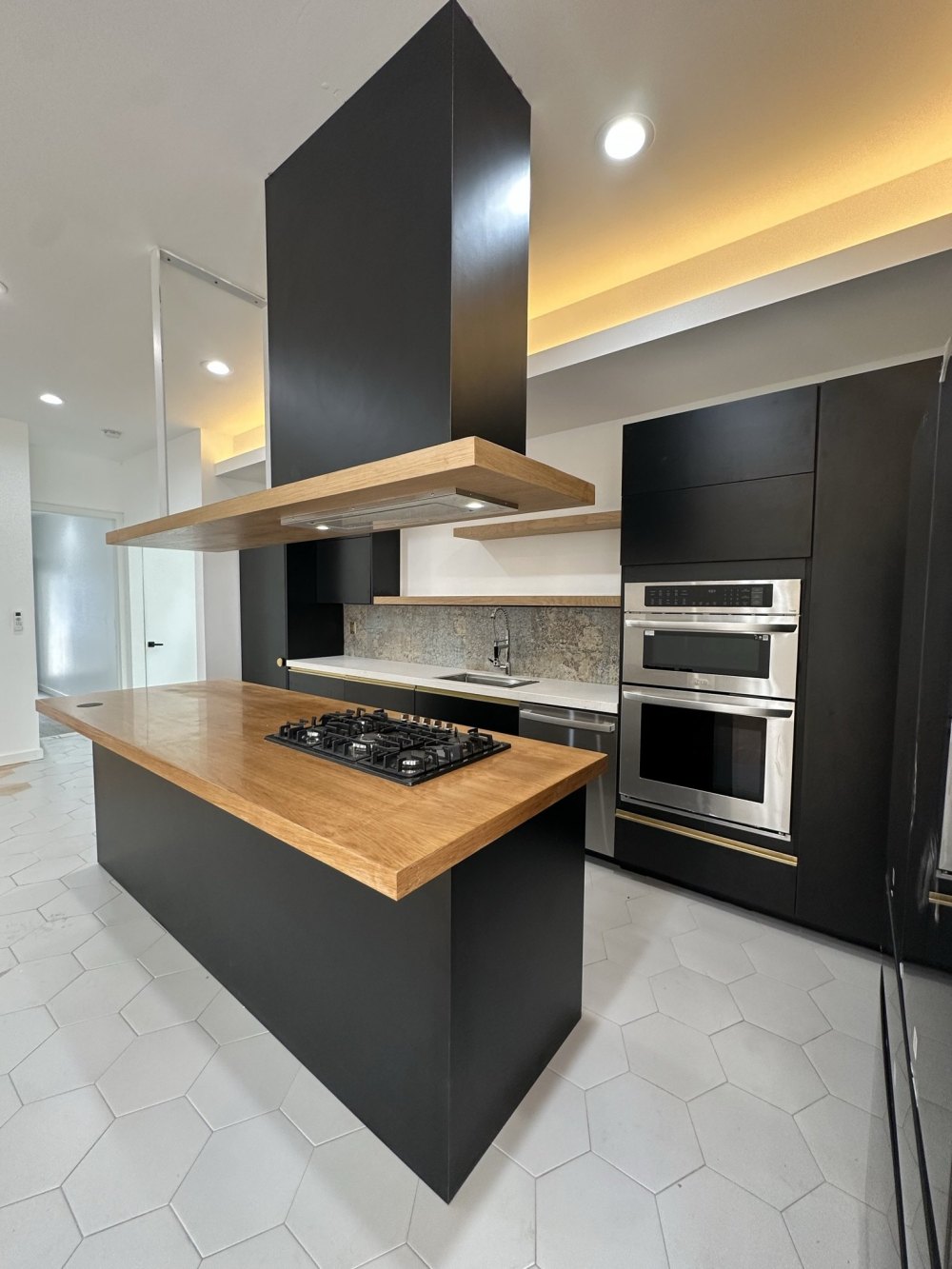 Matte black kitchen with a white oak island and floating oak hood, built by X-Trim Cabinets